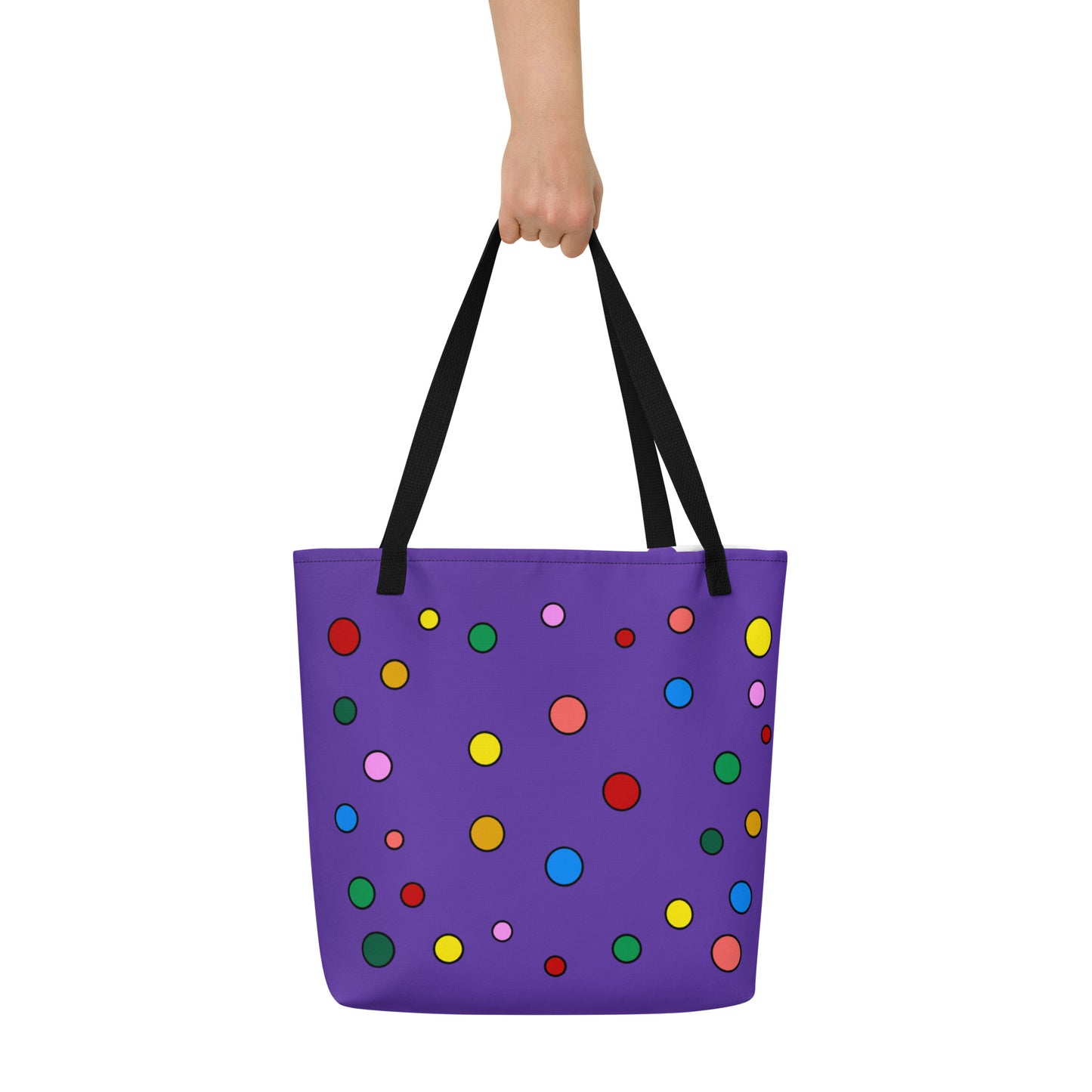 full frontal view of bold purple tote bag with rainbow polka dot design being held by its black straps. 